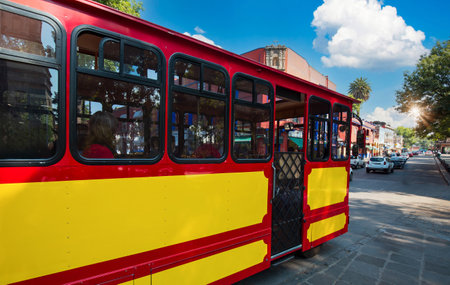 Tour Bus going on beautiful colonial and colorful Coyoacan Streets near Mexico City on city tourの写真素材