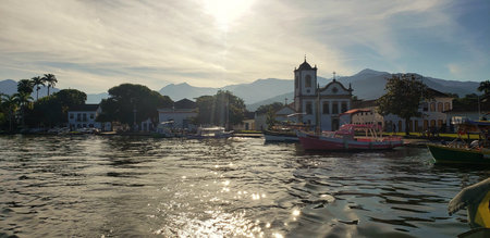 Church in the background where several boats are parked next to a beautiful pink boat in a setting with a mountain in the background and a beautiful sunset under white clouds and aの写真素材