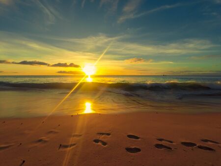 Footsteps on the beach with a warm sunsetの写真素材