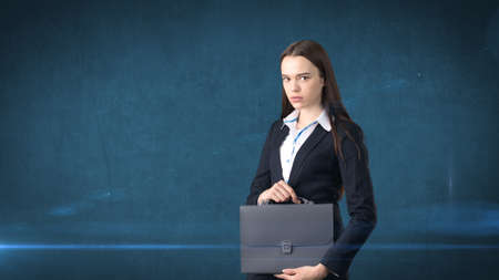 Young serious beautiful businesswoman portrait with gray briefcase, dark backgroundの写真素材