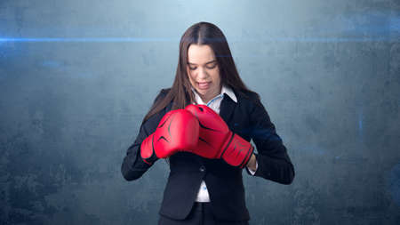 Young beautiful woman in black suit and white shirt standing in combat pose with red boxing gloves. Business concept.の写真素材