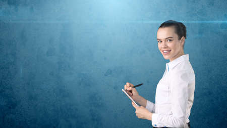 Professional confident businesswoman with bun writing in her organizer isolated on studio background. Business concept.の写真素材