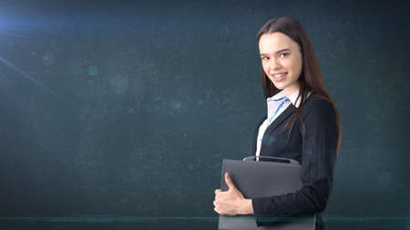 Young beautiful businesswoman portrait with gray briefcase, dark backgroundの写真素材
