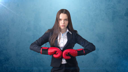 Young beautiful woman in black suit and white shirt standing in combat pose with red boxing gloves. Business concept.の写真素材