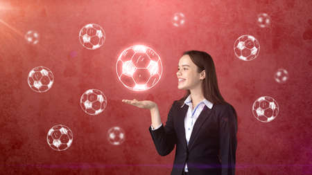 Portrait of young woman in suit holding soccer ball on the open hand palm, drawn studio background. Business concept.の写真素材