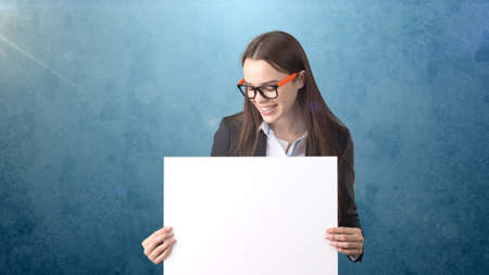 Smile Business woman portrait with blank white board on blue isolated . Female model with long hair in glasses.の写真素材
