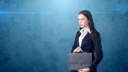 Young serious beautiful businesswoman portrait with gray briefcase, dark backgroundの写真素材