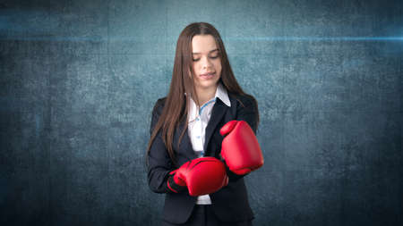 Young beautiful woman in black suit and white shirt standing in combat pose with red boxing gloves. Business concept.の写真素材
