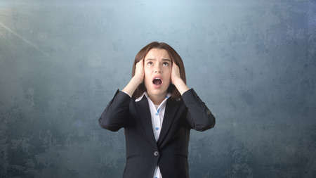 Young attractive longhair businesswoman in suit stressed, screaming and holding her ears, isolated studio backgroundの写真素材