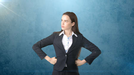 Young business woman in black suit and white shirt is standing, holding her hands on hips. Isolated. Blue background.の写真素材