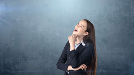 Smiling businesswoman with arms folded looking up at copyspace. Standing over gray background.の写真素材