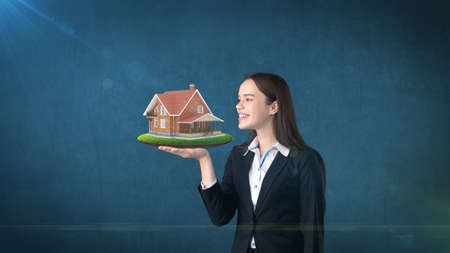 Portrait of woman holding rustic wooden house on the open hand palm, over isolated studio background. Business concept.の写真素材