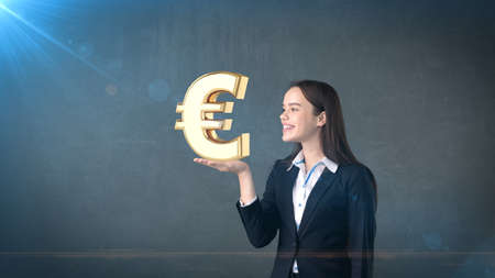 Portrait of woman holding golden euro sign on the open hand palm, over isolated studio background. Business concept.の写真素材