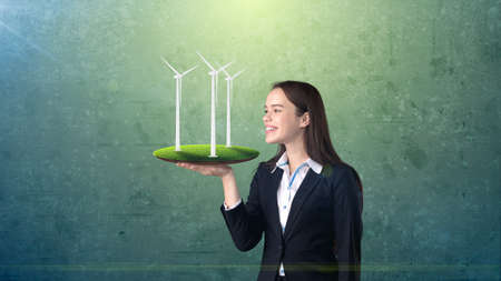 Portrait of young woman holding windmill on the open hand palm, over isolated studio background. Business, eco concept.の写真素材