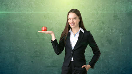 Girl in business suit holds bright vibrant apple in hand, symbolising new ideas and fresh concepts or healthy lifestyle in the office. Isolated studio backgroundの写真素材
