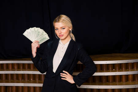 Beautiful blonde businesswoman with money at loft office in black suit.