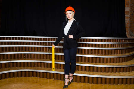 Beautiful blonde businesswoman with tape measure at loft office in orange glasses and black suit. Business concept.の写真素材