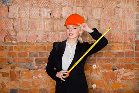 Beautiful blonde businesswoman with application tier at loft office in orange construction helmet and suit.の写真素材
