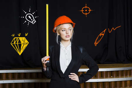 Beauty blonde businesswoman with designer or architect staff is standing against concrete wall with startup sketch on itの写真素材