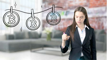 Surprised smiling young woman wearing a suit and looking at a cryptocurrency sketch on a design flat wall. Concept of Bitcoin risk.の写真素材
