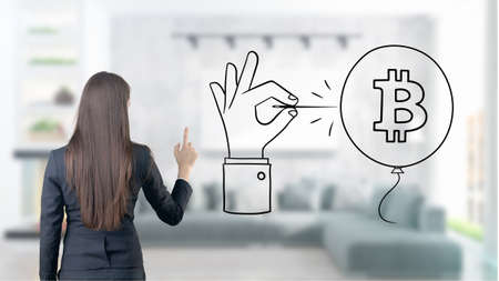 Surprised smiling young woman wearing a suit and looking at a cryptocurrency sketch on a design flat wall. Concept of Bitcoin risk.の写真素材