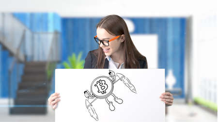Surprised smiling young woman wearing a suit and looking at a cryptocurrency sketch on a design flat wall. Concept of Bitcoin risk.の写真素材
