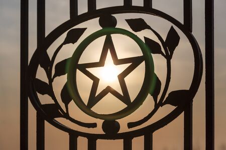 The forged star in laurel leaves and branches (wreath) against the background of the sun in kontrovy...