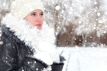 The young woman in a white cap, mittens and a sheepskin coat the tinsel decorated New Year's with ornament on the street in the winterの写真素材