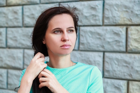 The woman the brunette in a blue light jacket against the background of a gray wall looks aside. A...