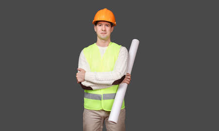 the civil engineer in a helmet holds drawings, documents in hand, looks in the camera