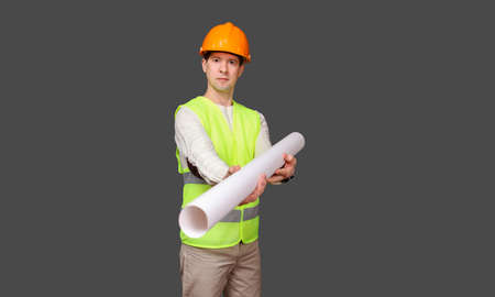 the civil engineer in a helmet and a vest, stretches drawings forward