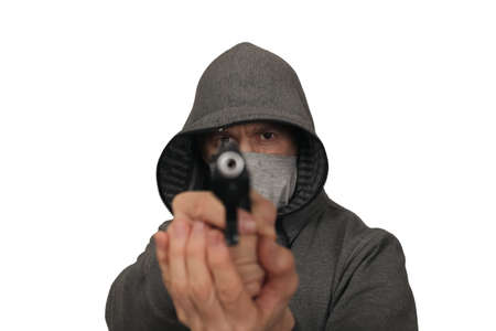 The man and in a mask on a face keeps a gun in a sports jacket before himself. A white background, a portrait on a beltの写真素材