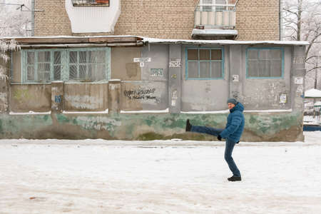 The man in a winter jacket and a cap goes on snow a wide step against the background of the houseのeditorial素材