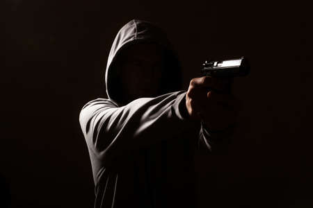 the resolute silhouette of a man without a face threatened to fire, holds a gun in his hands, against a black background, isolatedの写真素材