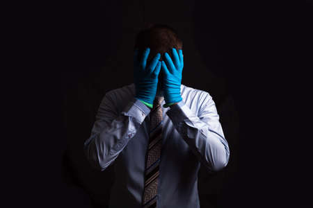 business man doctor in stress grabbed the head with two hands, mask shows a foot gesture, on a dark background, isolatedの写真素材
