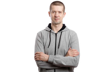 A sports strong athlete is a man, wearing a hooded jacket, his arms crossed on his chest. A look into the camera. Isolated, on whiteの写真素材