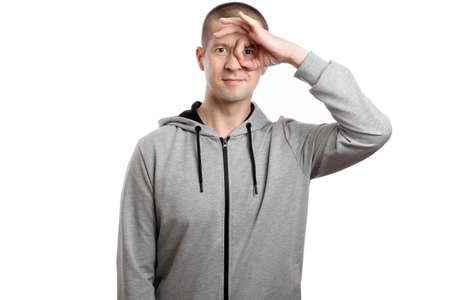 happy successful man, wearing a hooded jacket, shows the OK sign or okey, with a hand brush in his eye. A look into the camera. Isolated, on whiteの写真素材