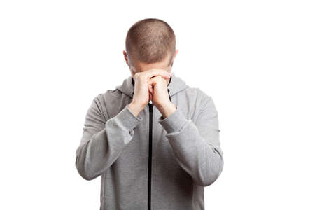 faithful praying male athlete in prayer folded his hands together to each other, his head lowered to the bottom. Dressed in a gray hooded jacket, short haircut. Isolated, on whiteの写真素材
