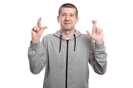 Hopeful man in anticipation crossed his fingers, dressed in sportsclothes, isolated, on whiteの写真素材