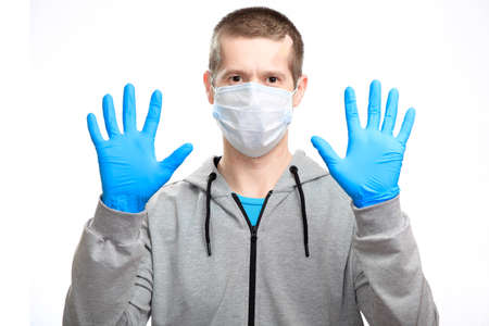 A sports man in a medical mask shows rubber gloves put on his hands, a stop gesture, wearing a sports jacket, staring at the camera. Close-up isolated on whiteの写真素材