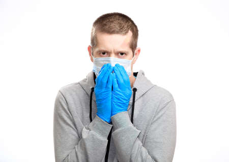 sick cold man sneezes, closed his mouth and nose with his hands. Dressed in a medical mask, rubber gloves, sports jacket, looks into the camera. Close-up, isolated, on whiteの写真素材