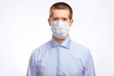 A serious man in a medical mask, a light shirt looks into the camera. Isolated, on white