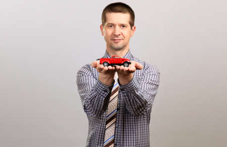 A manager in a cage shirt and tie holds a small car, shows. Isolated, grayの写真素材