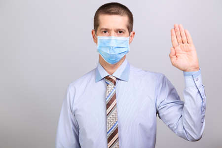 Man in shirt, tie and medical mask holds hand at top on head level, isolatedの写真素材