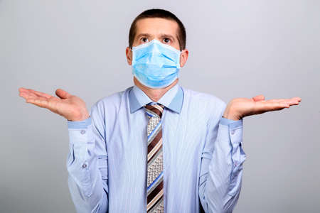 Business man in medical mask spreads his hands in the sides and looks upの写真素材