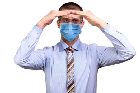 Businessman in medical mask and glasses looks into the camera far away, holds hands with a houseの写真素材