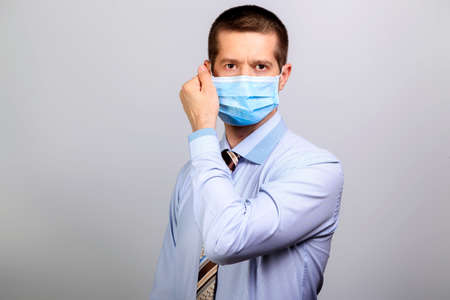 Recovered man in medical mask, shirt, tie removes maskの写真素材