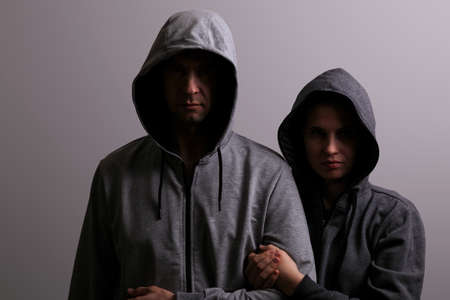 Man and woman in hoods stand by, low key, dark backgroundの写真素材