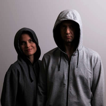 Man and woman in hoods stand by, low key, dark backgroundの写真素材