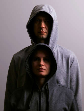 Man and woman in hoods stand by, low key, dark backgroundの写真素材